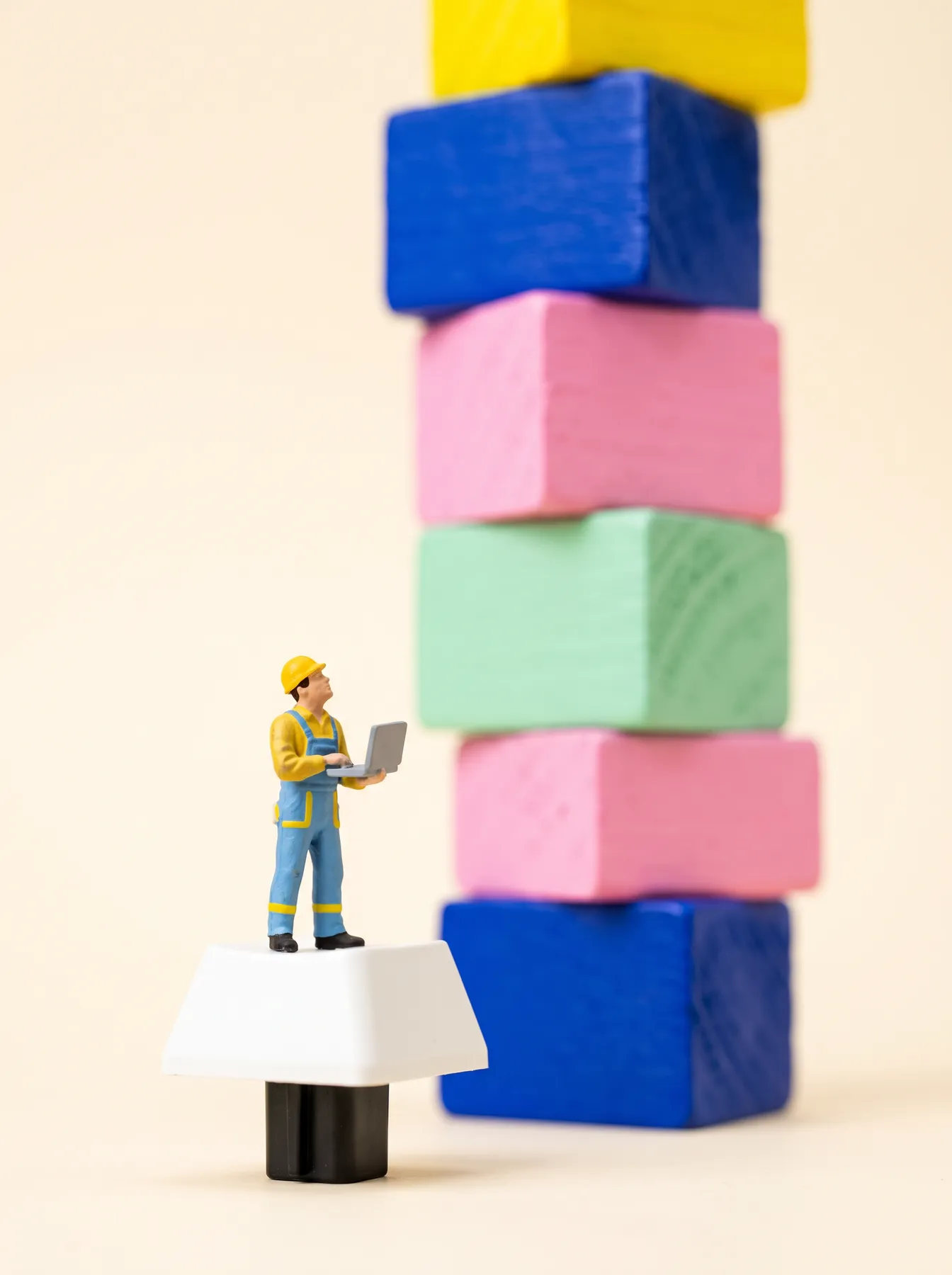 A tiny figurine engineer on a keyboard key, looking up at a tower of blocks